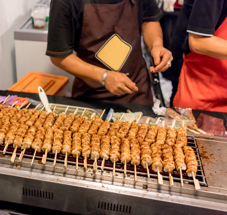 Hands moving around grilled marinated pork on wooden stick on hot modern stove.の写真素材