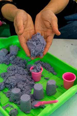 Woman hands holding kinetic sand and letting go into mini plastic bucket. Mother and kid indoor play.の写真素材