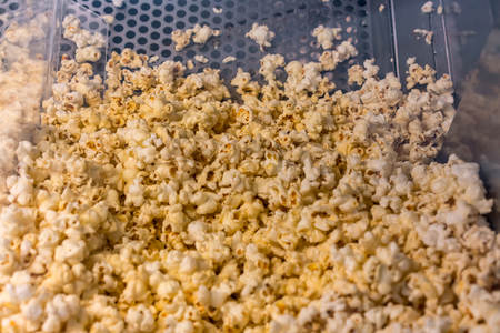 A closed up look through glass cabinet of salted butter popcorn in incubator machine at movie counter bar.の写真素材