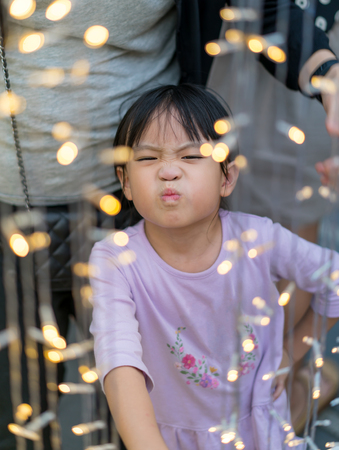 Asain kid girl with funny face and Chrismas lightihng decoration foregroundの写真素材