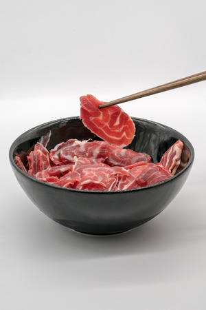 Chopstick holding fresh sliced beef hind shank from black ceramic bowl isolated on white backgroundの写真素材