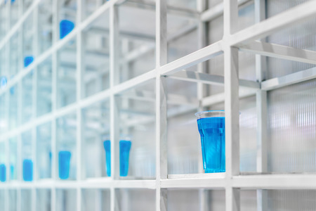 Blue water inside clear plastic cup on white metal shelf structure for decoration. Installation art concept.の写真素材