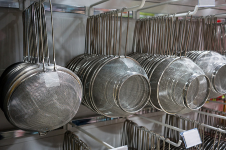 Many rows of silver metal colanders and strainers hanging on metal rack in wholesale store.の写真素材