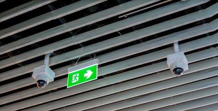 Green emergency exit sign. Direction to the escape way and CCTV hanging on wood ceiling.