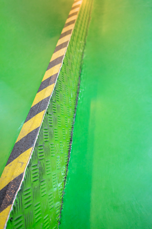 Industrial striped road or step warning on green walkway. yellow-black pattern.の写真素材