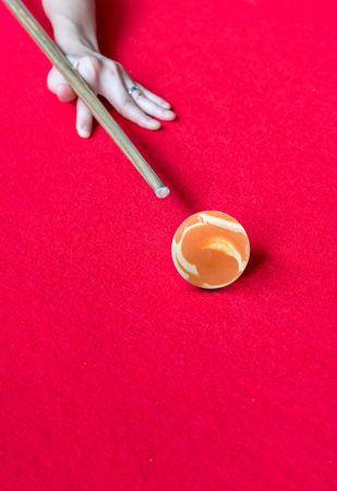 hand aiming the orange marbel cue ball on red billiard table.