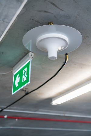 Electric wires in aluminum pipes running across the concrete ceiling and facility system under neon light in parking lotの写真素材