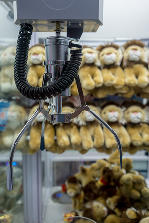Mechanic claw crane for grabbing soft toy in doll vending machine at game center. Robotic arms with clamp over plastic dispenser for controller.の写真素材