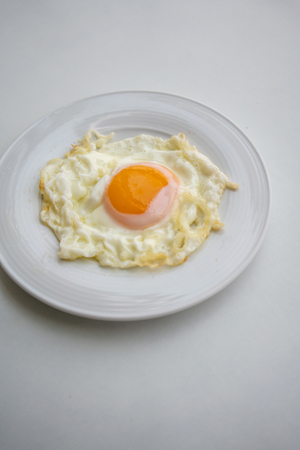 Fried egg on white ceramic dish or plate isolated on white background. Healthy breakfast food.の写真素材
