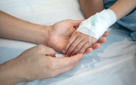 Mother hands holding her baby patient hand with Saline intravenous or (IV) drip.の写真素材