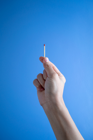 Woman hand holding a match stick against blue background.の写真素材