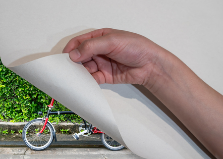 Kid's hand open paper corner revealing bicycle with nature view. Travel concept.の写真素材