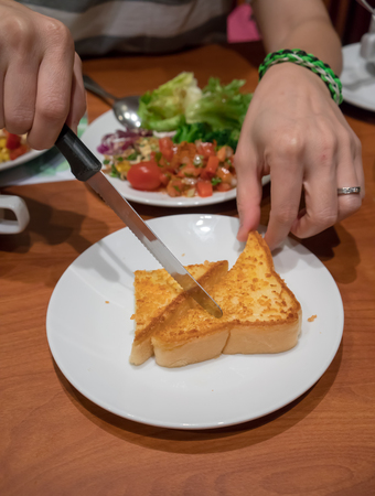 Hands using knife to cut toasted butter bread serving with vegetable salad. Selective focus.の写真素材