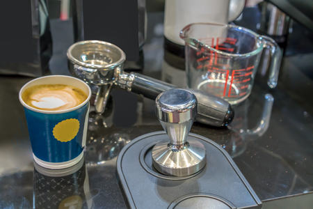 Morning coffee in blue cup by clean stainless steel tamper and portafilter on counter bar.の写真素材