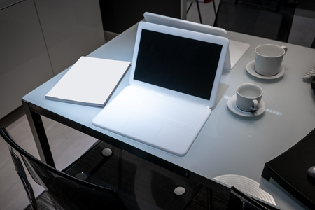 Modern white office desk table with laptop computer with black screen, book and cup of coffee.の写真素材