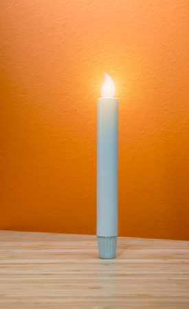 LED candle light standing on wooden table isolated against yellow orange background.の写真素材