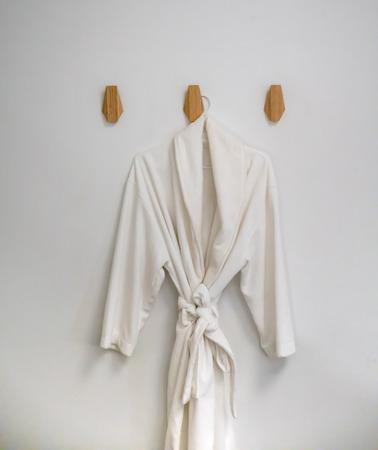 Classic bathrobe hanging on wooden abstract wall hook mounted against white wallの写真素材