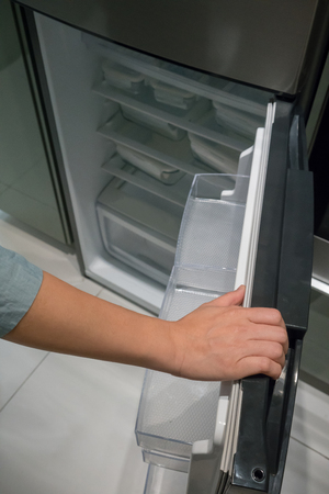 Closed up hand opening the silver color handle of monochromatic refrigerator door.の写真素材