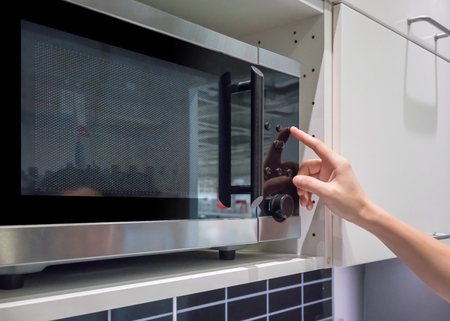 Woman's hands pressing button on black microwave for cookingの写真素材
