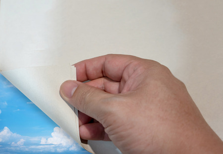Man's hand open paper corner revealing nature blue sky view. Travel concept.の写真素材
