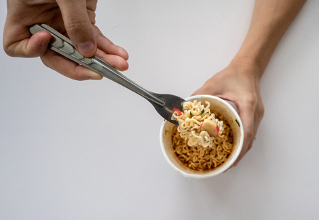 Hand uses fork to pickup tasty instant noodles isolated on white backgroundの写真素材