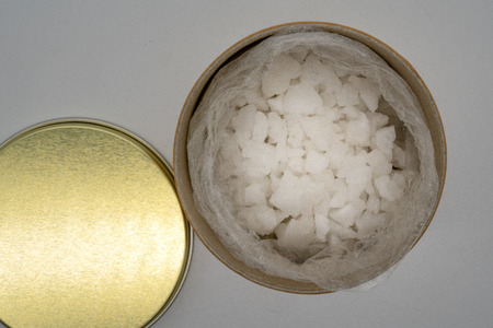 Sea salt in plastic bag kept in open recycled cylinder container by its golden lid isolated on white...