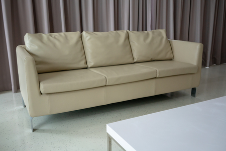 New white leather couch on white floor against light brown fabric curtain.