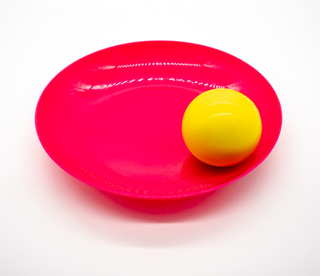 Yellow ball on red and pink plastic dish isolated on white backgroundの写真素材