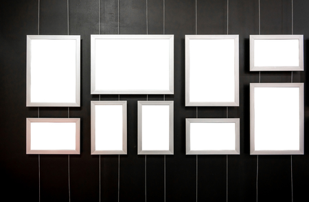 Blank aluminum picture frames hanging on metal sling against black wall background.