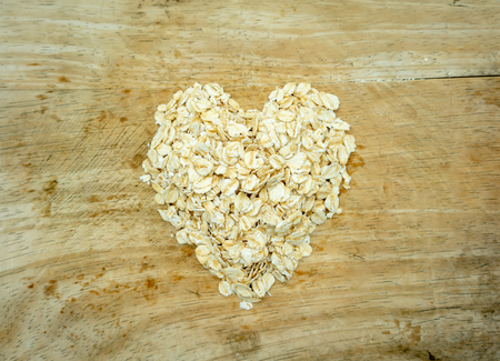Dry rolled oats flakes pile in heart shape on wooden board. Healthy food ingredient for love and care.の写真素材