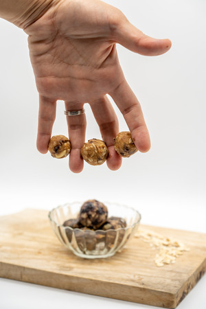 Four fingers holding mini homemade peanut butter energy balls against blurred healthy power balls in glass bowl background. No bake recipe.の写真素材
