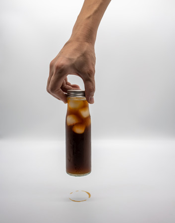 Hand holding a glass bottle of coffee with ice isolated on white background