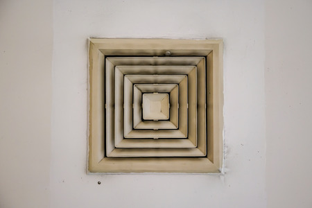 Old and dirty air duct vent hole fan on ceiling in building or home ventilation systemの写真素材