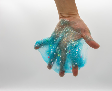 Hand playing or soaking transparent blue glitter slime isolated on white backgroundの写真素材