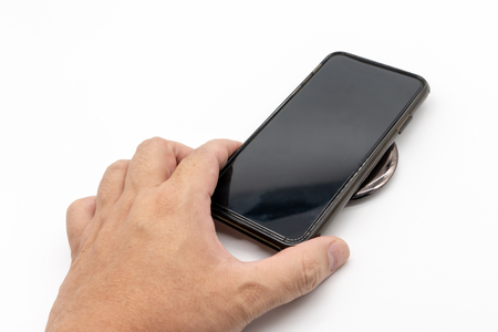 Hand holding black mobile phone to charge on the black grossy round shape wireless charger isolated on white background.の写真素材