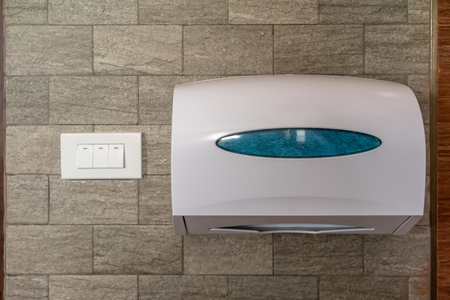 White box of tissues hanging on stone tile wall near electric switches in toilet or restroomの写真素材