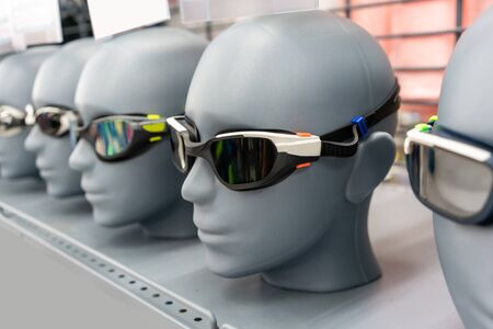 Colorful swimming glass for adult on grey human face model in store shelf.