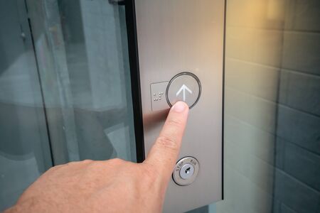 Male forefinger pressing on button up in front of the elevator in office building.