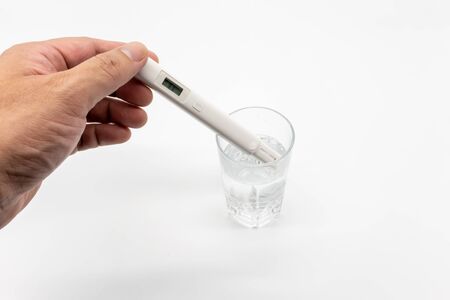 Hand holding white digital water TDS tester measuring in drinking water to determine water quality...