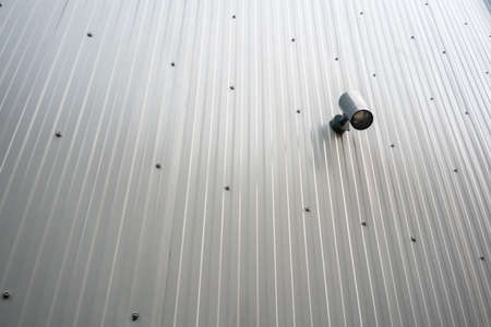 Black spot light hanging on metal sheet wall on outdoor public area.