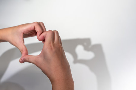 Kid hands creating silhouette shadow of heart on white wall background. Hand shadow of heart. Love or Valentine concept.の写真素材