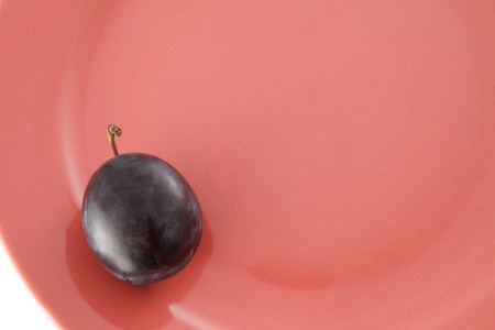 One ripe plum with stem on pink plate. For inspector:There is not a noise artefacts. It is structure of material under glaze. Thank You.の写真素材