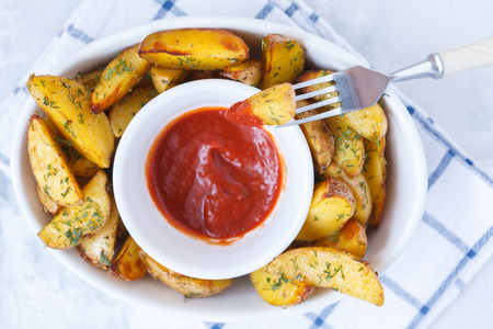 Baked potato slices with herbs in a white dish with tomato sauce, light background, top view. Vegan Healthy Food Concept.の写真素材