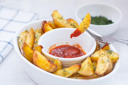 Baked potato slices with herbs in a white dish with tomato sauce, light background. Vegan Healthy Food Concept.の写真素材