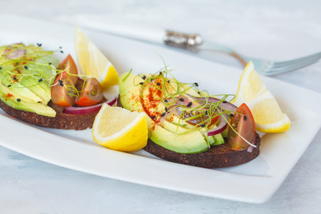 Sandwich with avocado, sprouts, tomato, light background.  Healthy green vegan breakfast concept.