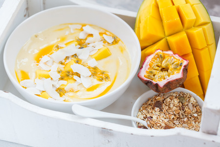 Mango smoothie bowl with coconut, granola and passion fruit in a white box. Healthy vegan diet breakfast concept.の写真素材