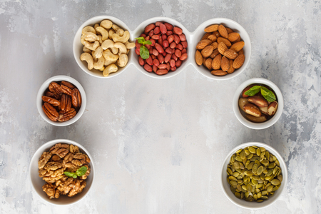 A variety of nuts and seeds in white bowls, top view, copy space, food background. Healthy vegetarian food concept.の写真素材