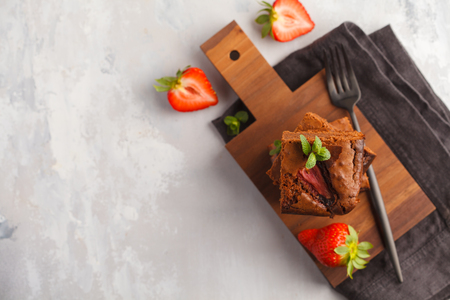 A stack of pieces of homemade dark chocolate brownie with strawberries on a wooden board. Top view, copy space.の写真素材