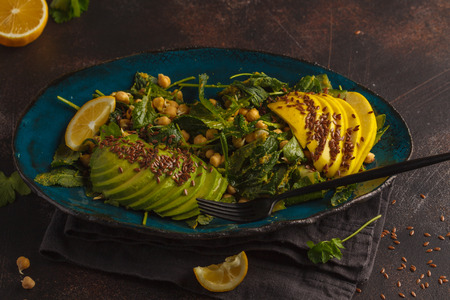 Healthy vegan avocado, chickpeas, kale salad in a vintage blue plate on a dark rusty background....