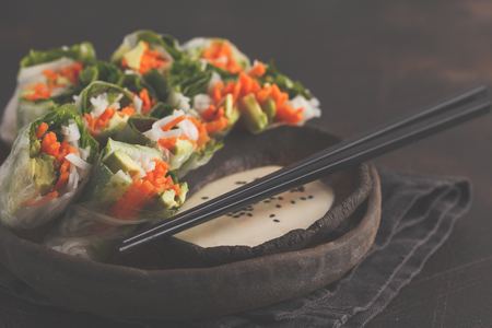 Fresh handmade vegan asian spring rolls with rice noodles, avocado, carrots and tahini dressing on black dishの写真素材